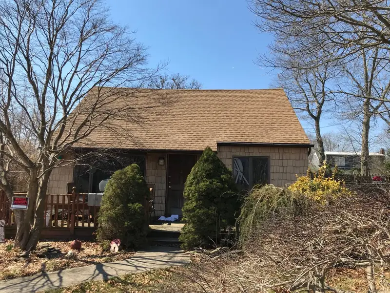 Shingled cape behind overgrown front shrubs, Shirley, NY